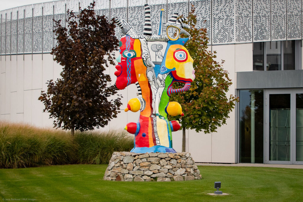 The sculpture 'Smiling Faces' by Belgian artist Bilio Nic - a vibrant, multi-colored contemporary totem-like sculpture in the middle of a manicured green lawn at Danubiana Meulensteen Art Museum near Bratislava, Slovakia