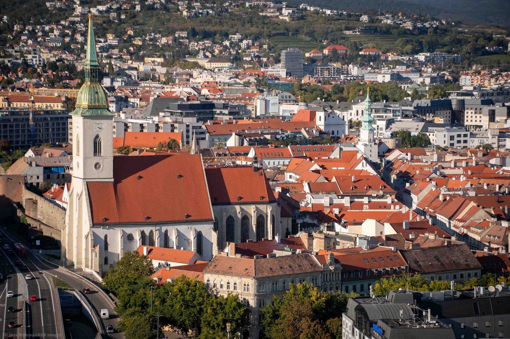 Wide-angle aerial shot of Bratislava Old Town on a clear day, showing St. Martin's Cathedral and other historic buildings with red roofs.